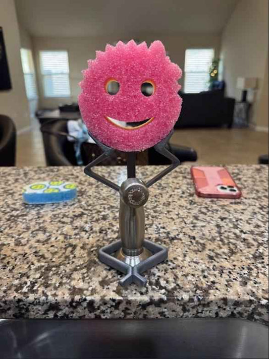 Stick figure sponge holder on a granite counter with a sponge